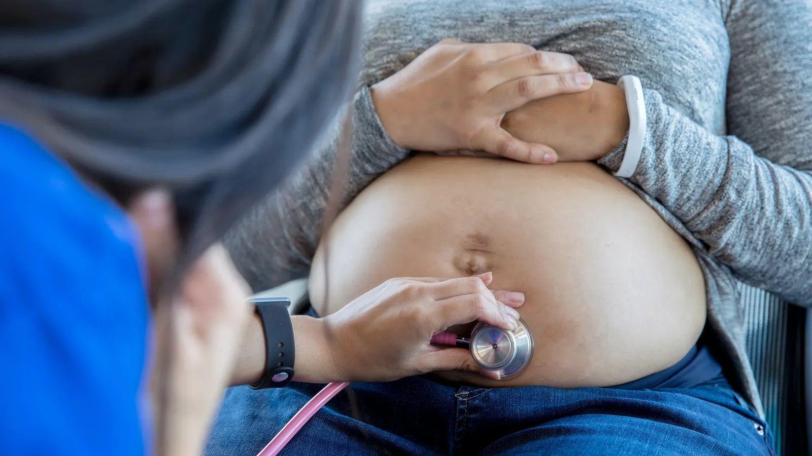Médica colocando estetoscópio em barriga de mulher grávida