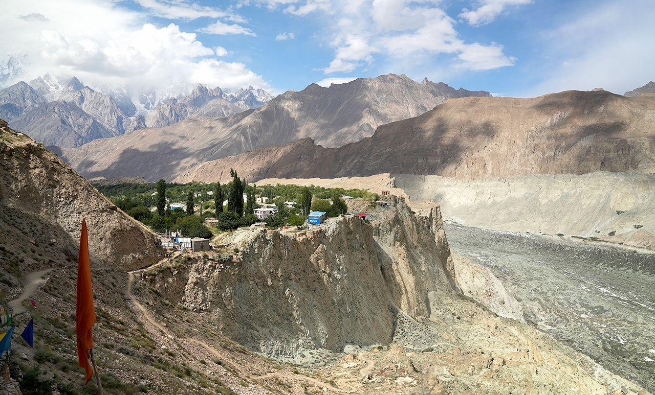 A village can be seen amongst trees with mountains and sky in the background, with the Hopper glacier running through the valley.