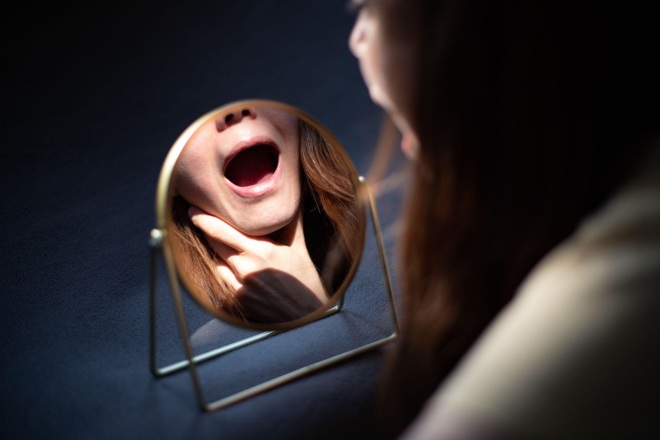 Mulher checando as amígdalas em espelho