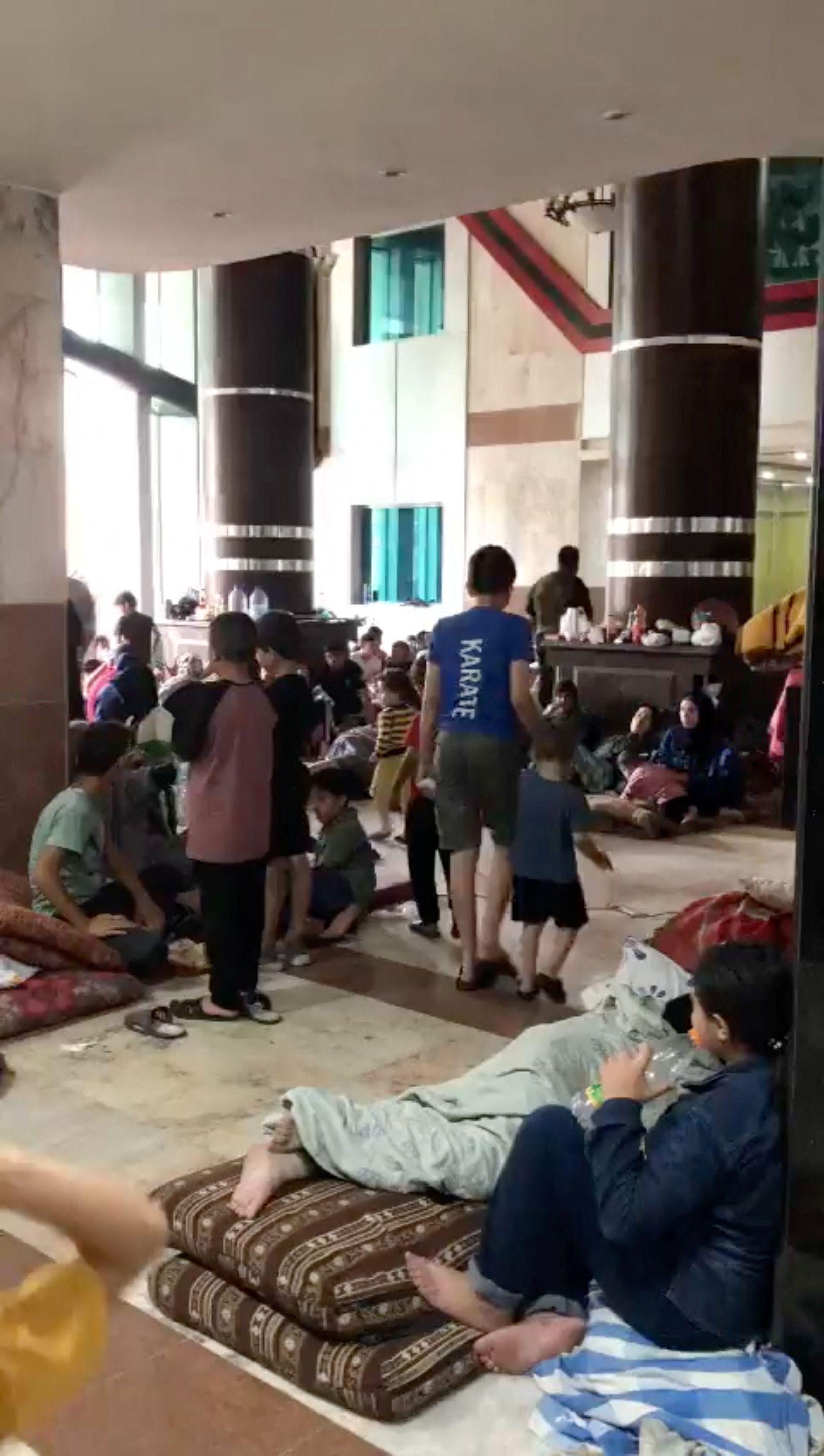 Gente distribuida en el suelo, sobre mantas, en lo que se parecia como una sala grande. 