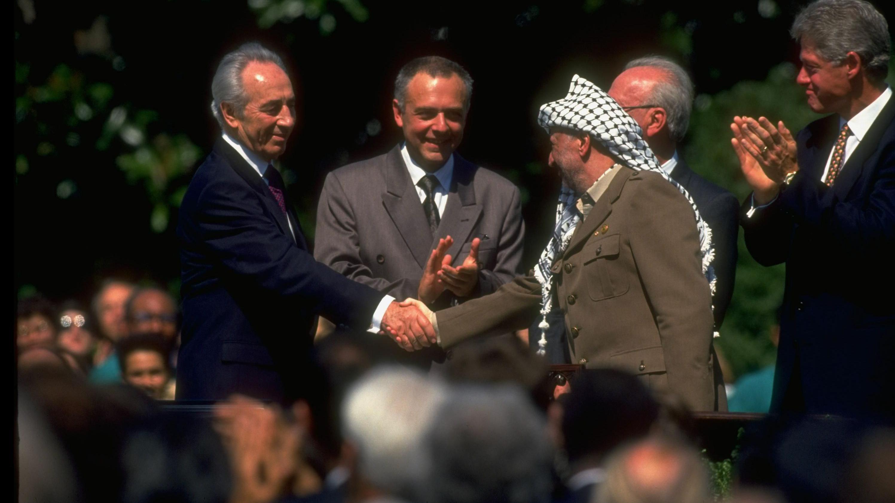 رئيس منظمة التحرير الفلسطينية ياسر عرفات (على اليمين) يصافح وزير الخارجية الإسرائيلي شيمون بيريز (على اليسار) خلال توقيع اتفاقية أوسلو.