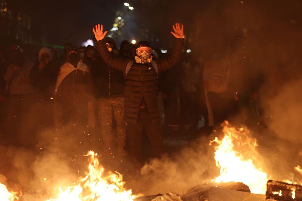 Manifestantes con las caras tapadas frente a fuegos en la calle. 