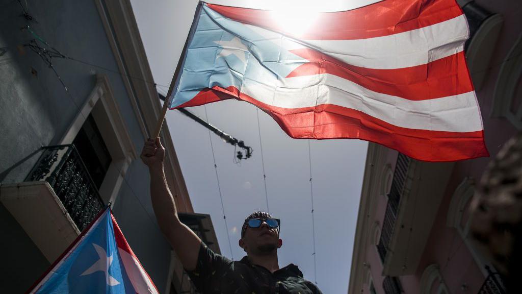 un hombre sostiene una bandera de puerto rico en el viejo san juan 