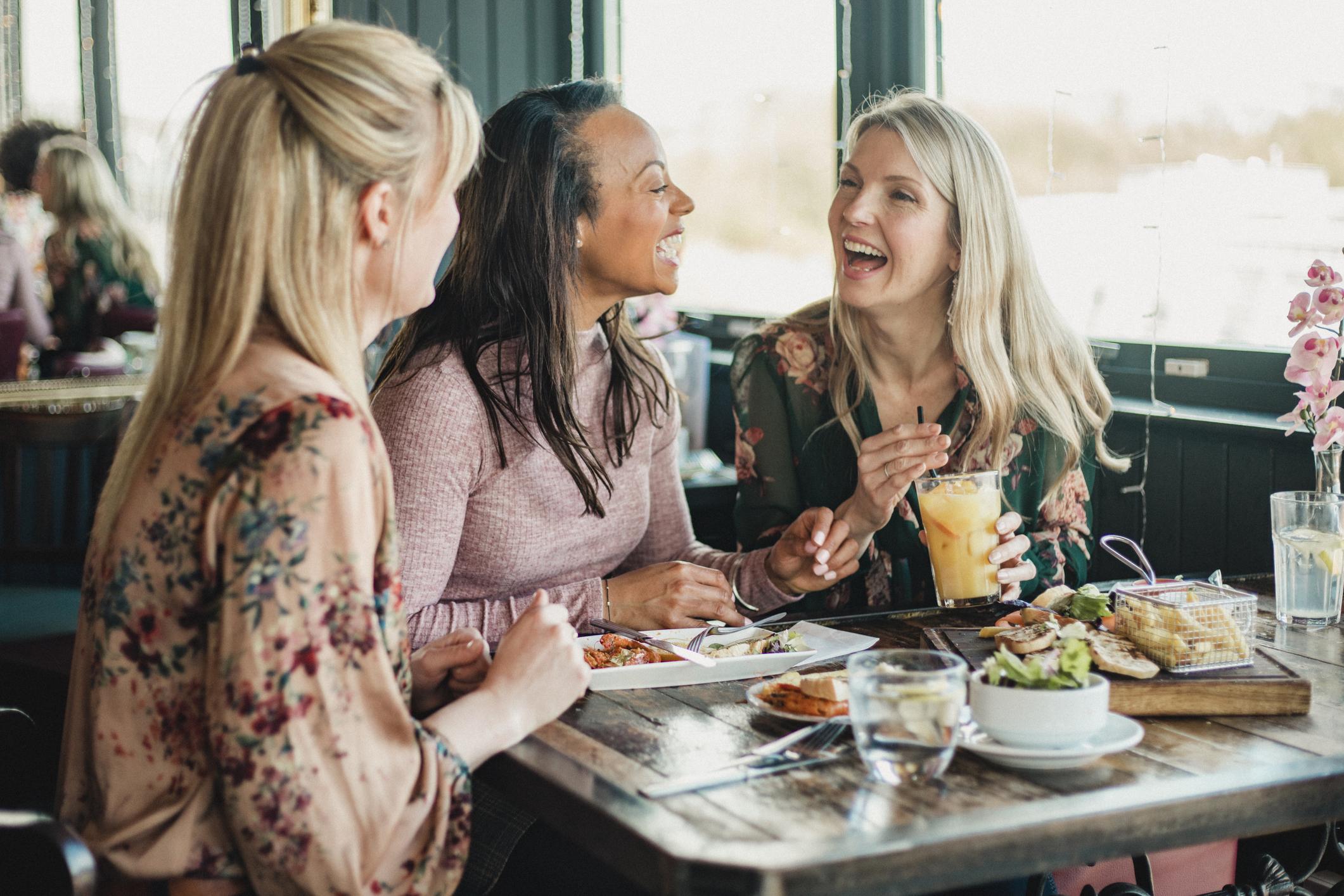 Três amigas rindo em restaurante