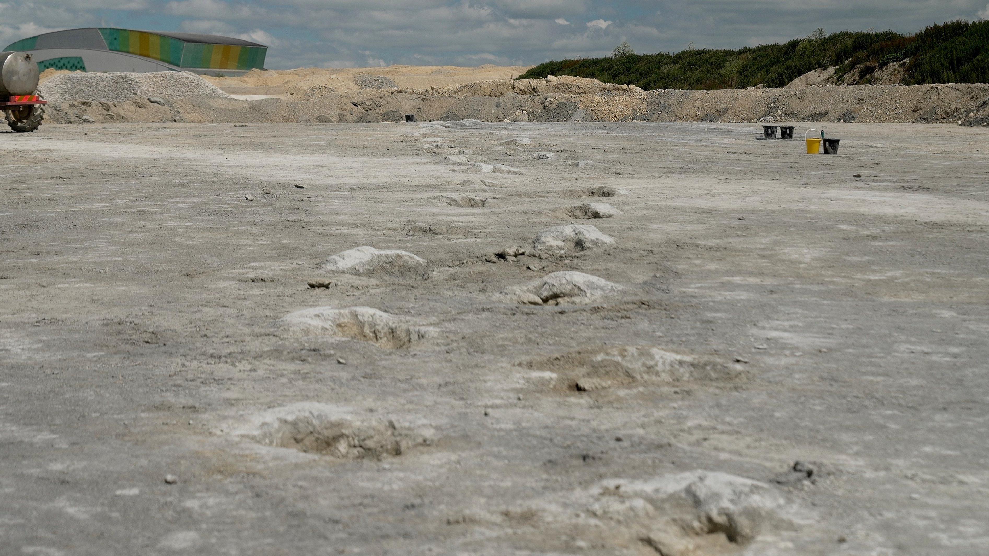 Veliki otisak dinosaurusa - poput velikih kratera u zemlji, u kamenolomu jasno pokazuje da je veliki dinosaurus hodao tim putem. U daljini stoje tri crne i jedna žuta kofa, što sugeriše da su ljudi radili sa strane. 