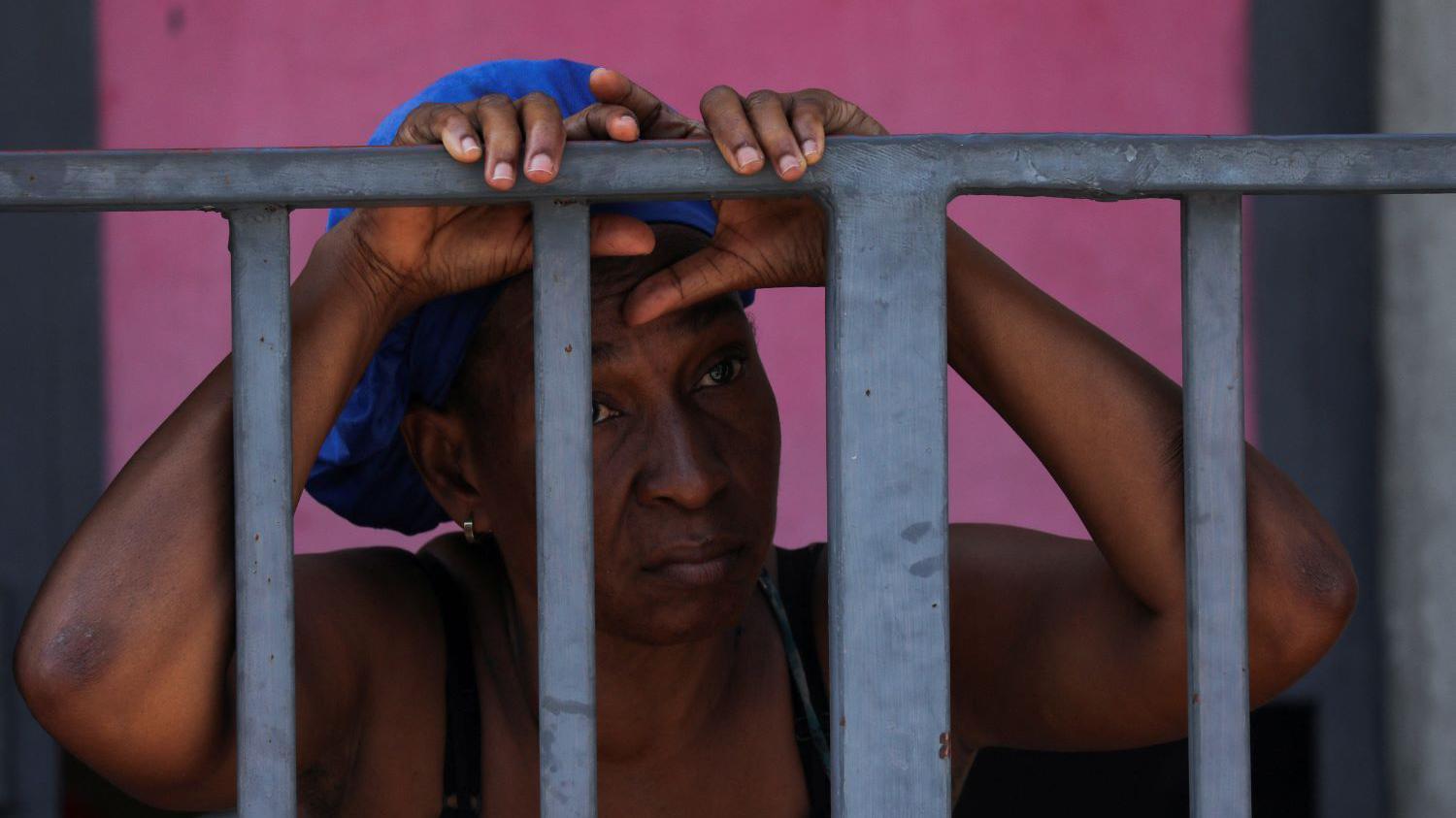 A woman looks mournfully out through the bars of a metal gate around a school building