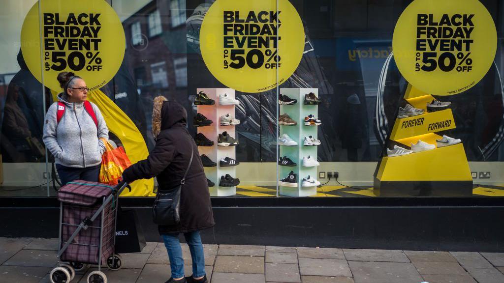 Foto mostra duas mulheres em frente a uma vitrine de tênis com anúnicos da Black Friday