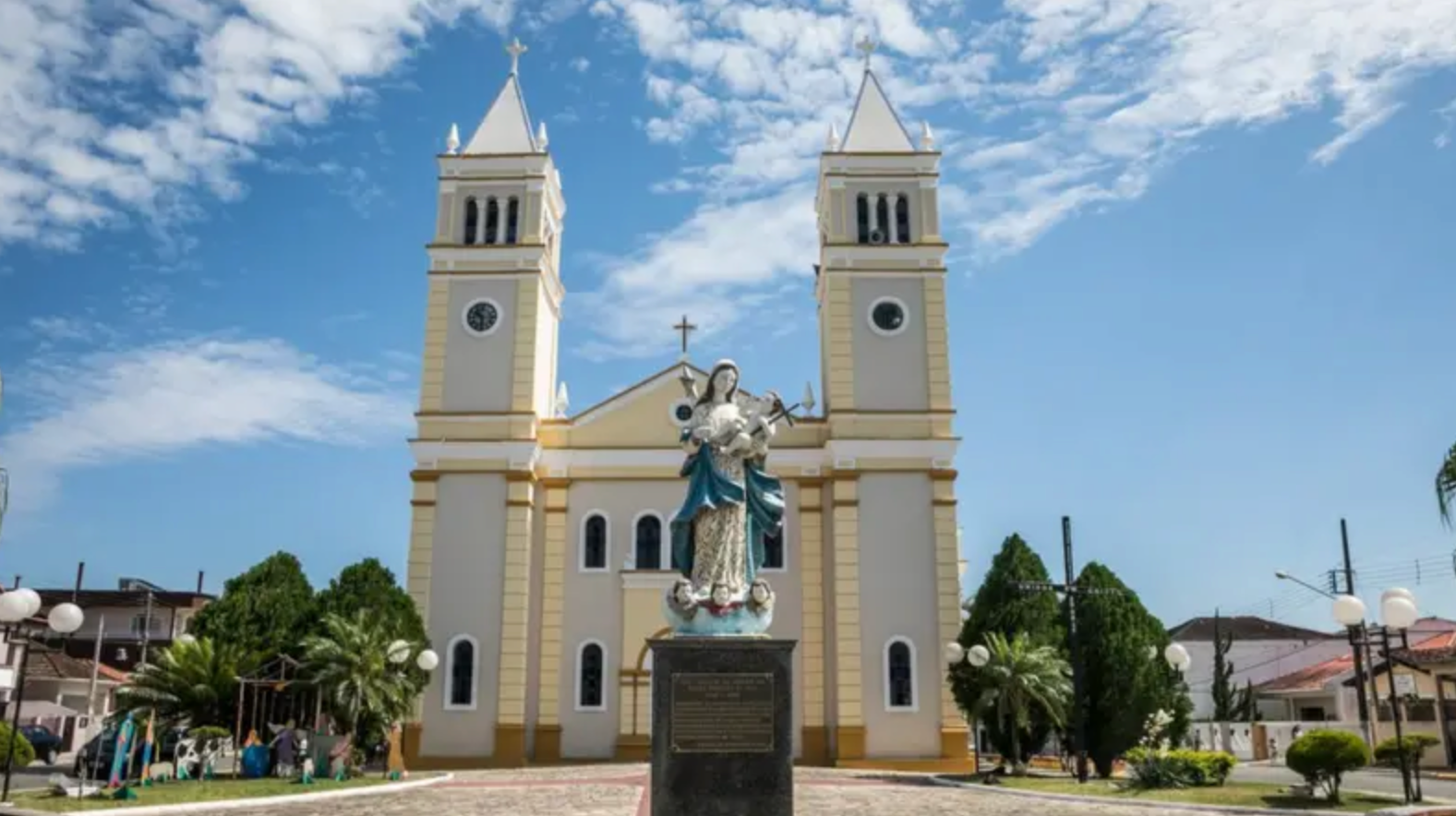 Imagem de Nossa Senhora em praça, com igreja católica ao fundo