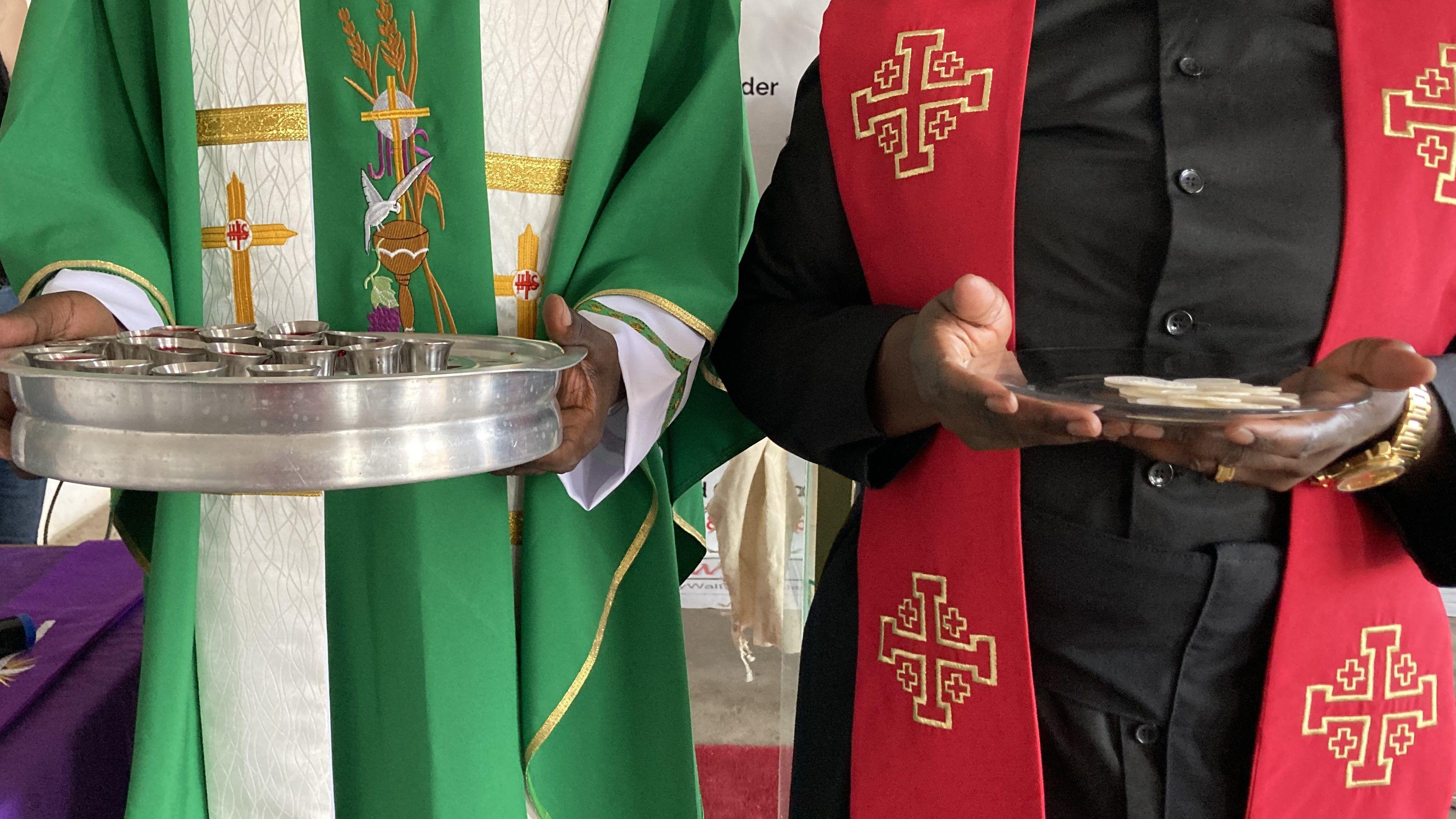 Dois clérigos seguram objetos sagrados (sem mostrar o rosto)