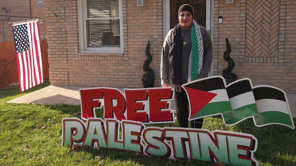 Laila Gaber frente a su casa que tiene una bandera de EE.UU. y una valla que lee "Palestina libre".