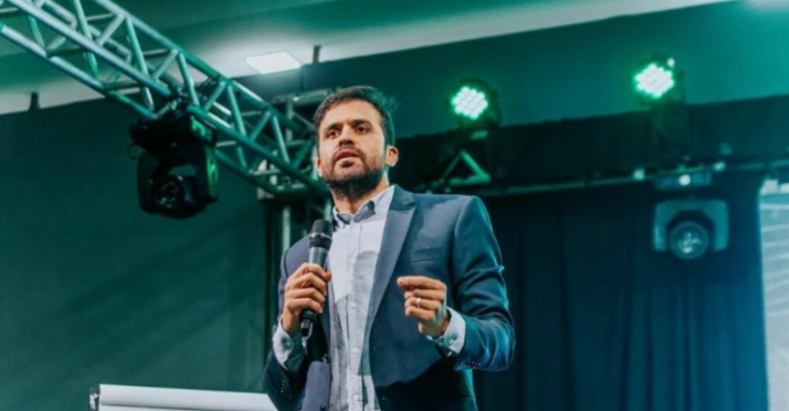 Pablo Marçal usando terno azul marinho em um palco durante palestra