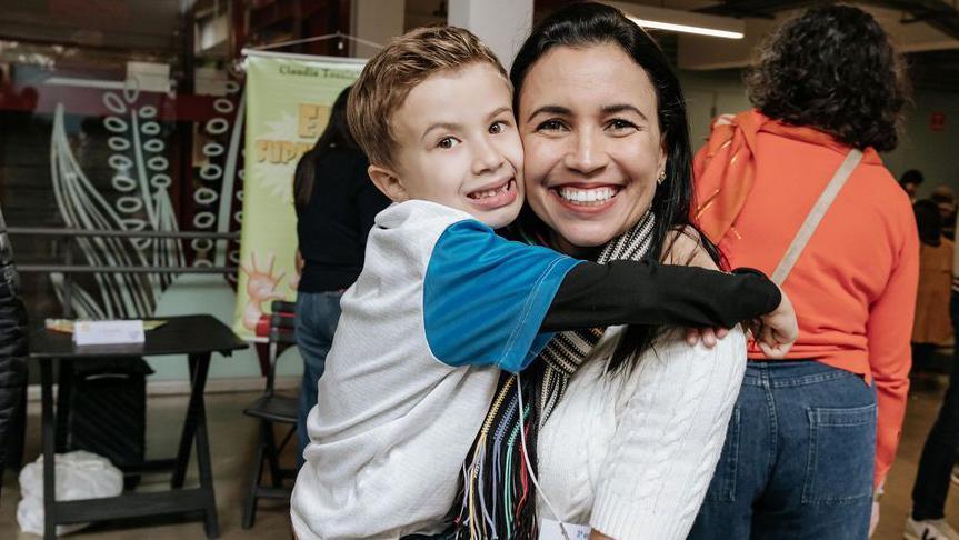 Roberta com filho no colo em evento da escola; ambos sorriem