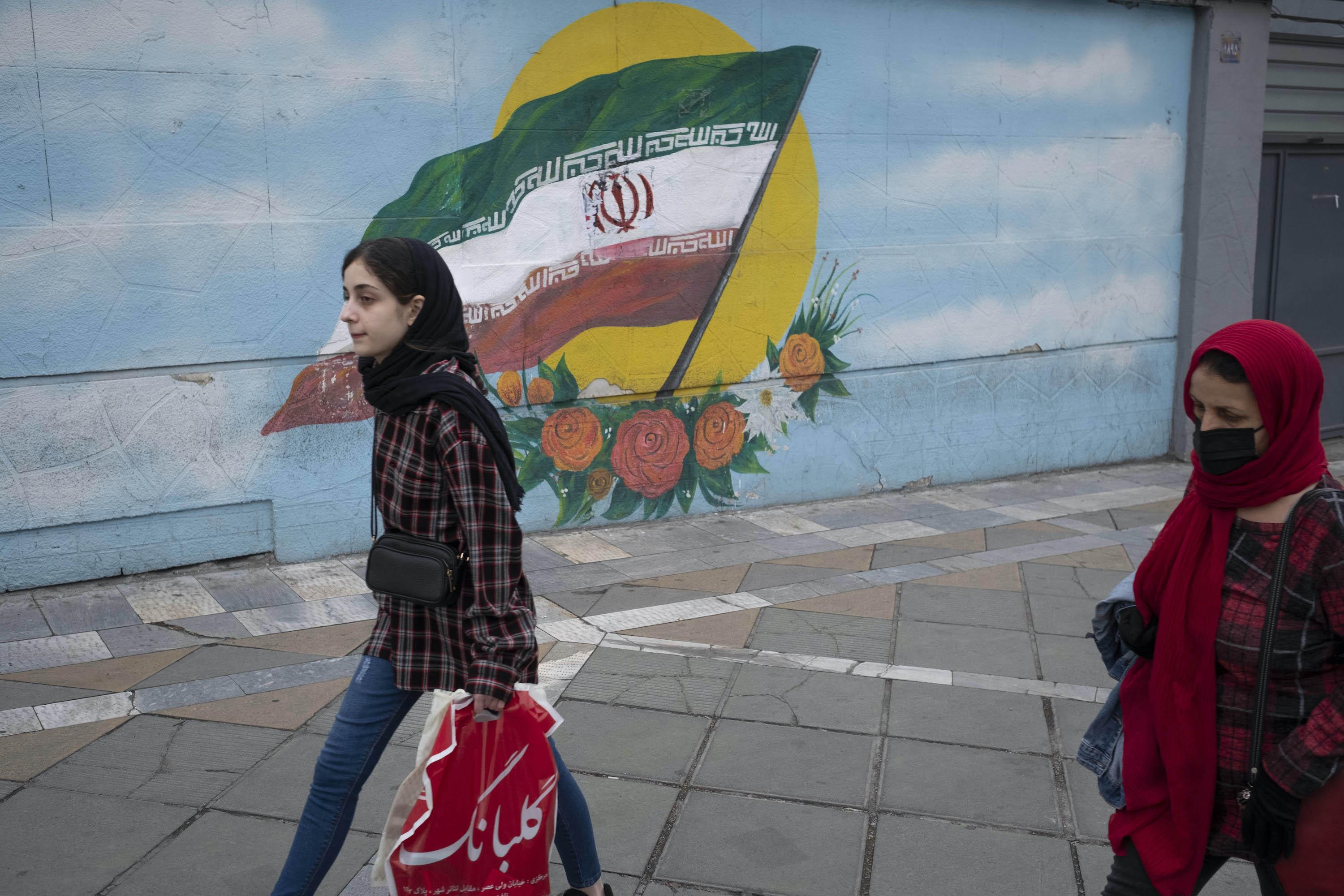Women walk past an Iran flag in downtown Tehran