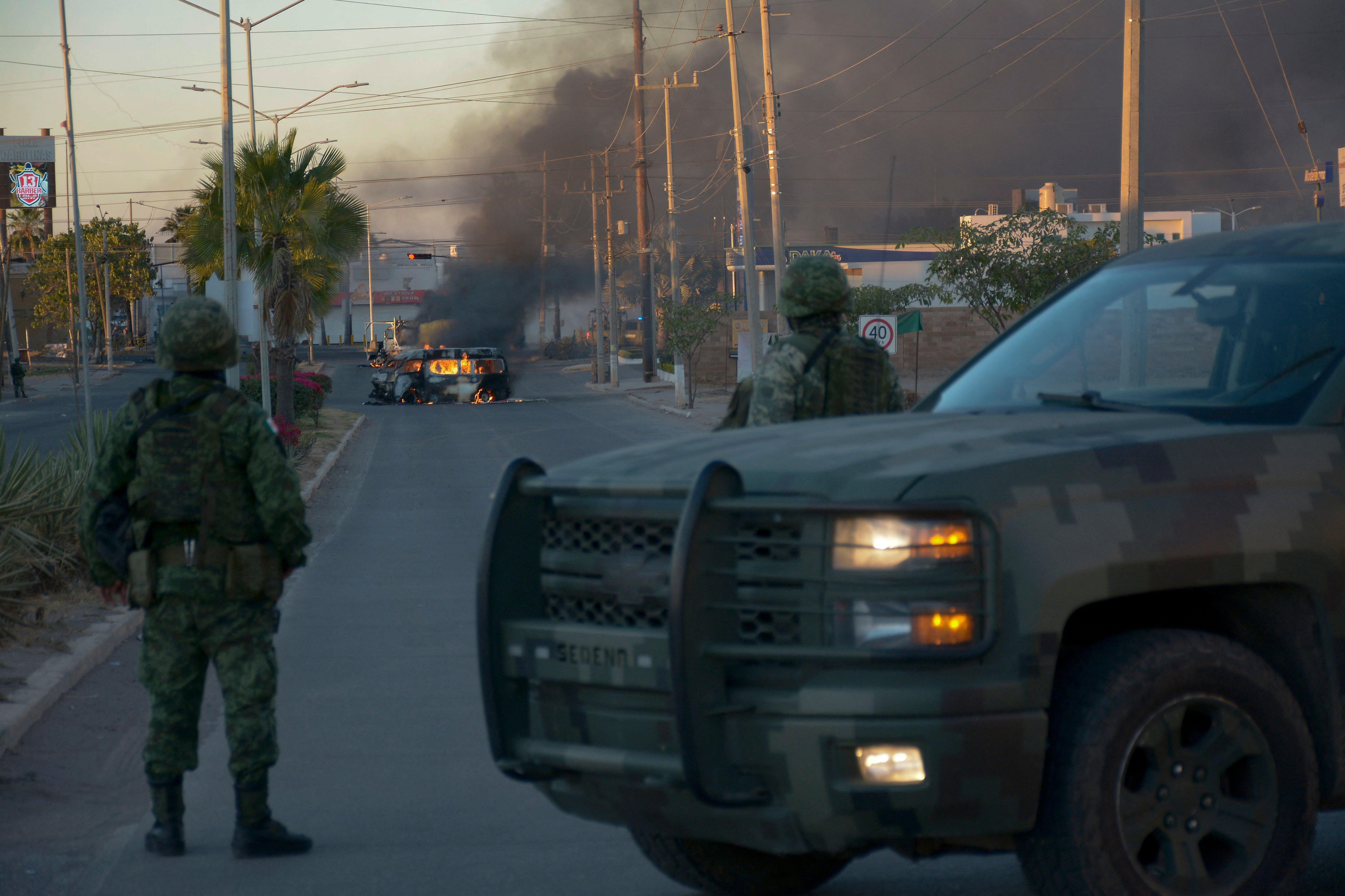 Dos soldados mexicanos obsarvan un vehículo incendiado en Culiacán, Sinaloa, debido a una ola de violencia narco en 2023.