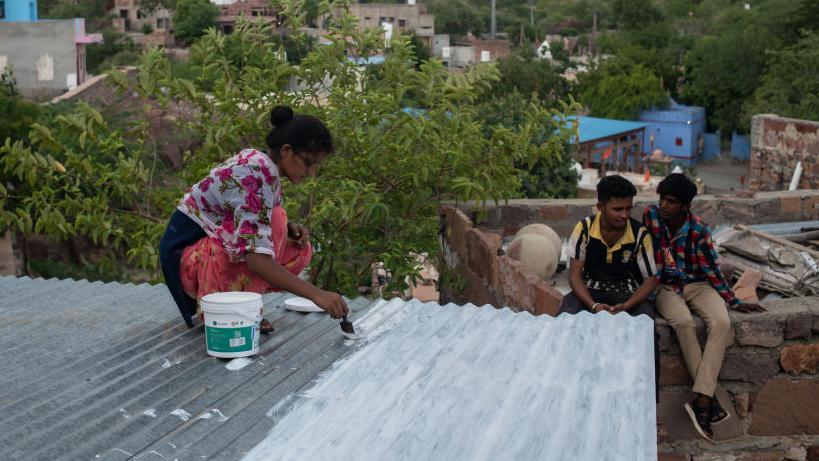 Seorang perempuan di Chandpole, Jodhpur, India, mengecat atap rumahnya dengan cat reflektif berwarna putih. 