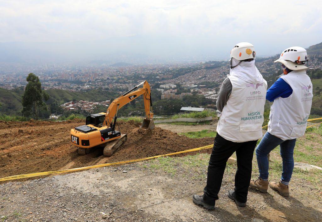 Dos expertos forenses observan el trabajo de una retroexcavadora