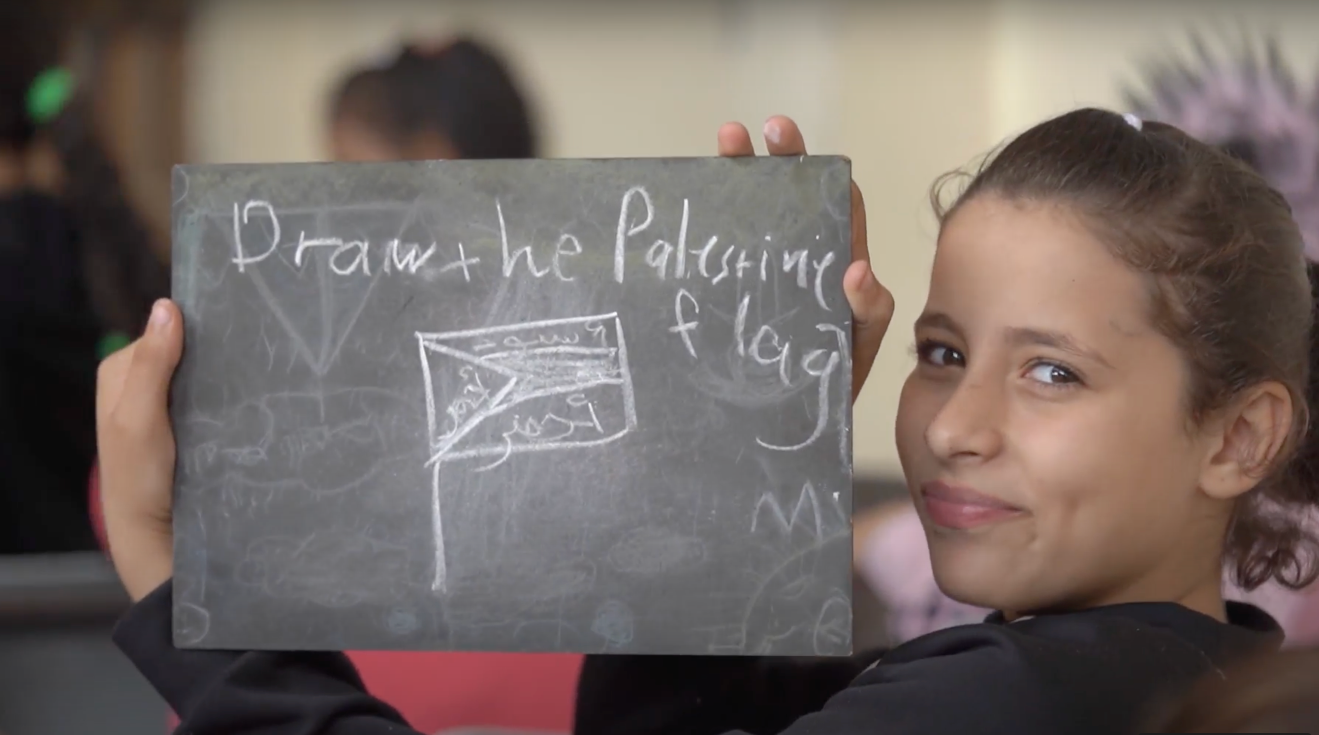 Una niña sosteniendo un tablero con el dibujo de una bandera palestina.