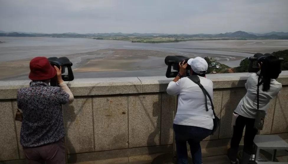 Turistas na Coreia do Sul olhando para o norte através da Zona Desmilitarizada que separa os dois países