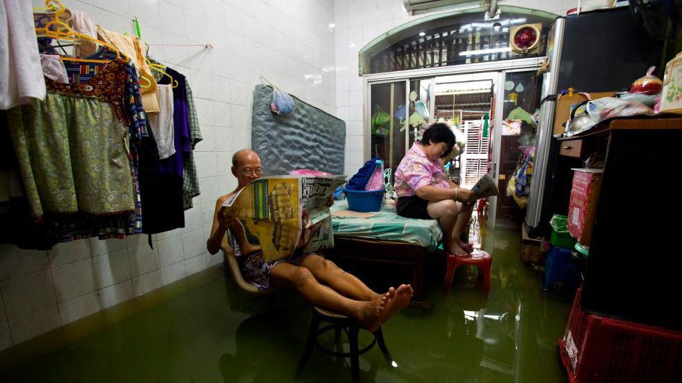 Duas pessoas lêem jornais dentro de uma casa inundada em Bangkok, perto do rio Chao Phraya, em 16 de outubro de 2011.