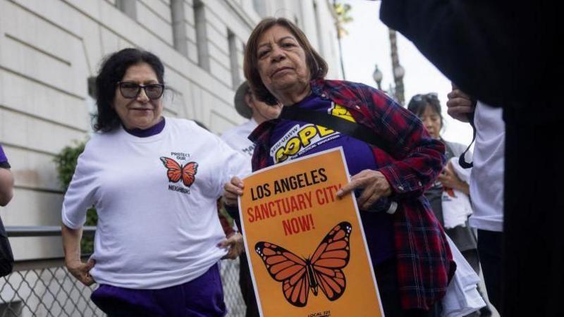 Duas mulheres, uma delas pedindo em cartaz que Los Angeles seja uma 'cidade santuário'