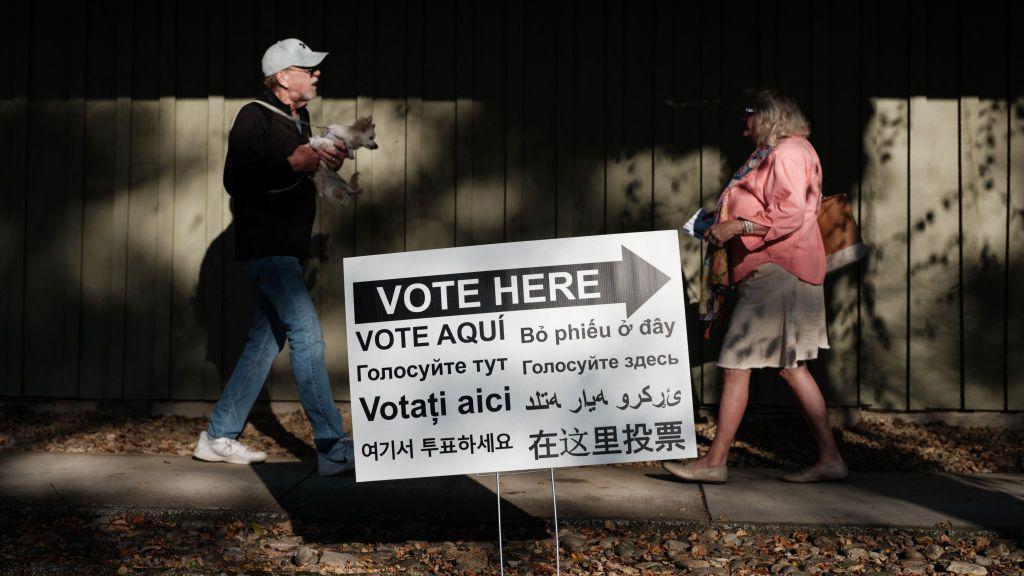 Un hombre y una mujer caminan delante de un cartel de votación en Estados Unidos con el mensaje en diferentes idiomas.