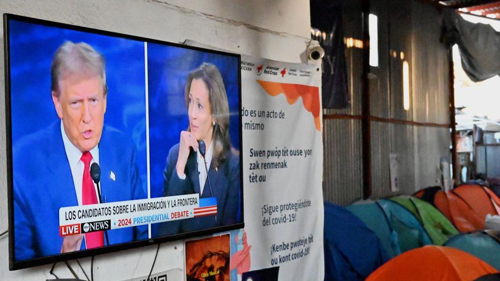 O primeiro debate entre Kamala Harris e Donald Trump é exibido na televisão do abrigo Juventud 2000, em Tijuana, no México, ao lado de tendas coloridas