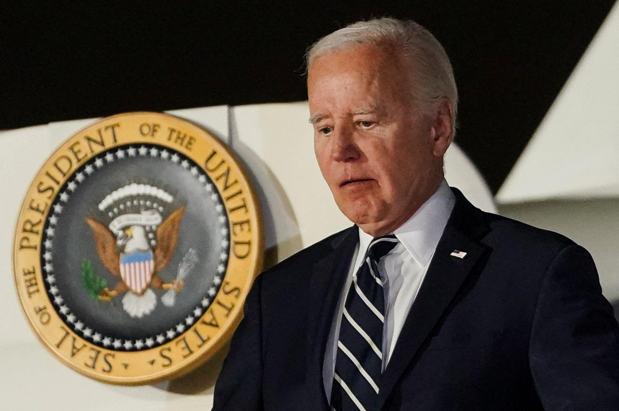 Joe Biden com feição séria ao lado de emblema da presidência
