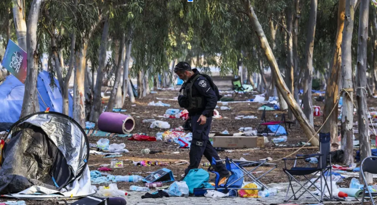 Policial uniformizado caminhando entre os escombros do ataque de 7 de outubro.