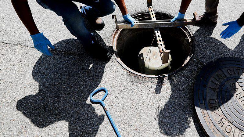 Trabalhadores manuseiam equipamento em bueiro.