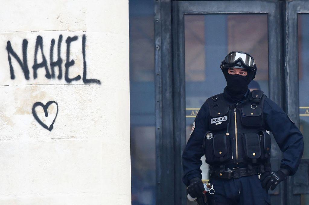Oficial de la policía nacional francesa asegura la entrada a un edificio junto al nombre 'Nahel', rociado en una columna durante las protestas en Nantes, en el oeste de Francia, el 30 de junio de 2023.