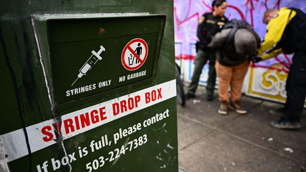 Uma caixa para descarte de seringas fica na rua enquanto um policial de Portland conduz uma investigação sobre tráfico de drogas e emite uma citação por posse de drogas durante uma patrulha no centro de Portland, Oregon, em 25 de janeiro de 2024