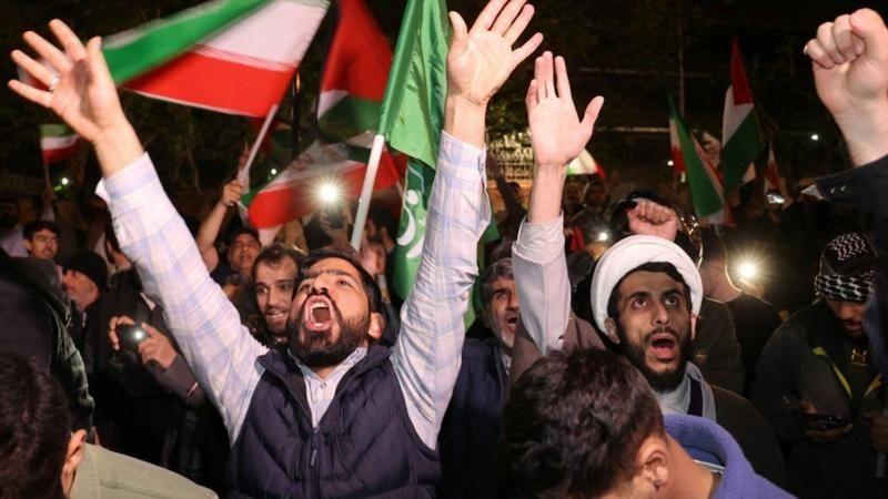 Fotografia mostra diveros homens árabes de barba gritando, com bandeiras do Irã em meio à multidão