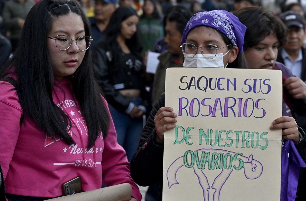 Don jóvenes, una de ellas con cartel que dice: "Saquen sus rosarios de nuestros ovarios"