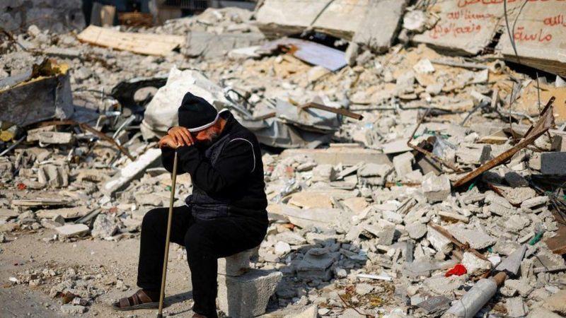 Homem sentado após destruição de prédio em Gaza