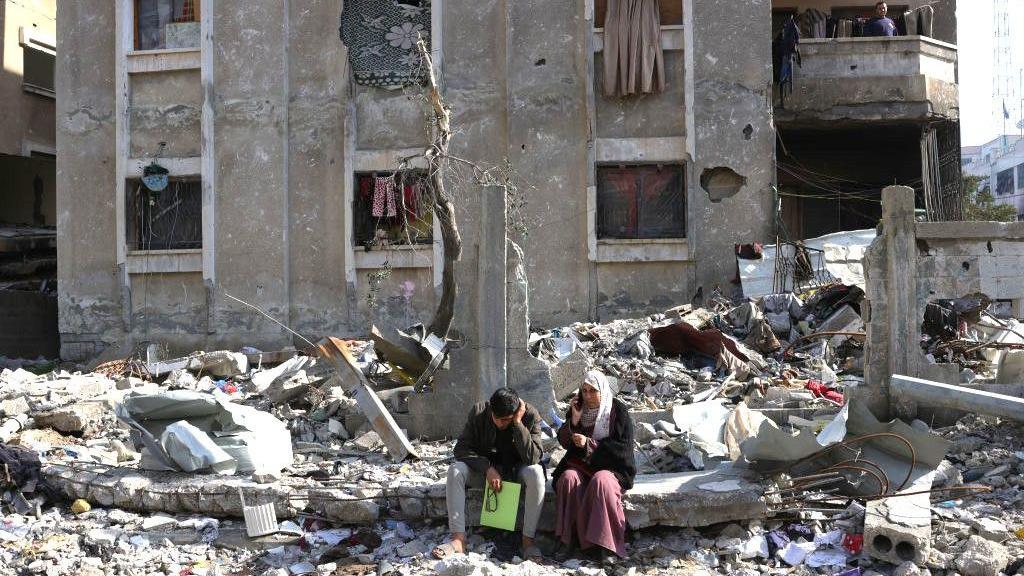 Warga Palestina duduk di luar rumah mereka yang hancur di bagian utara Jalur Gaza, 17 Februari 2025.