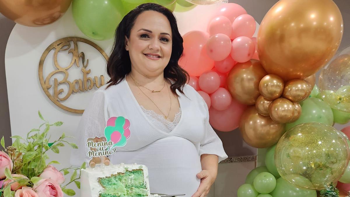 Luciene Alves de Melo grávida atrás de mesa com bolo em chá revelação