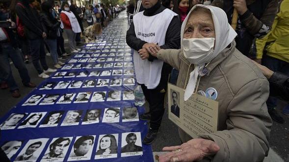 Adelina Lara Molina, integrante das Mães da Plaza de Mayo, ao lado de uma grande faixa com retratos de pessoas desaparecidas durante a ditadura militar argentina (1976-1983) 