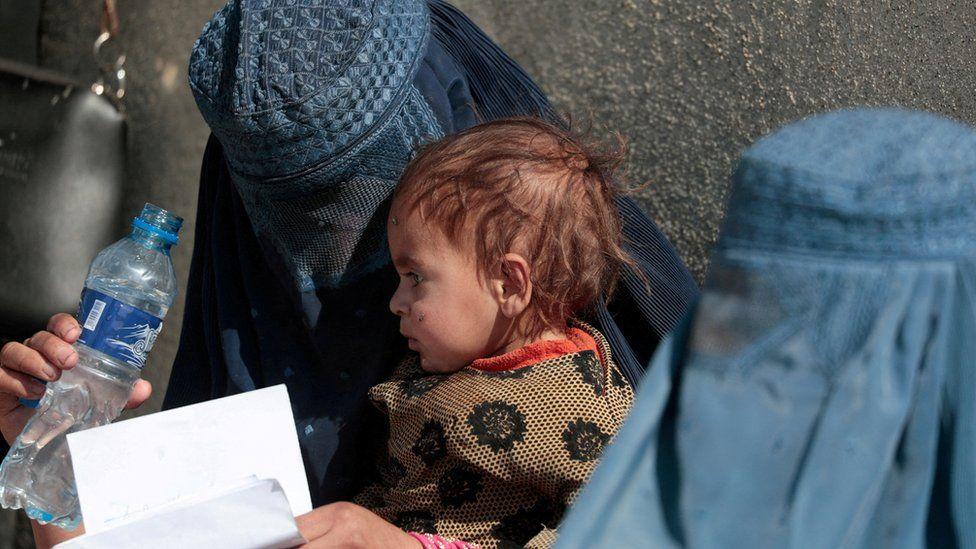 امرأة أفغانية نازحة تحمل طفلها بينما تنتظر مع نساء أخريات تلقي مساعدات خارج مركز توزيع تابع للمفوضية في ضواحي كابول