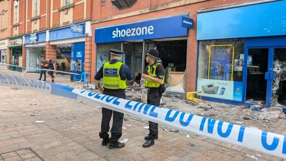 Police officers stand outside a smashed and raided Shoezone shop in Hull