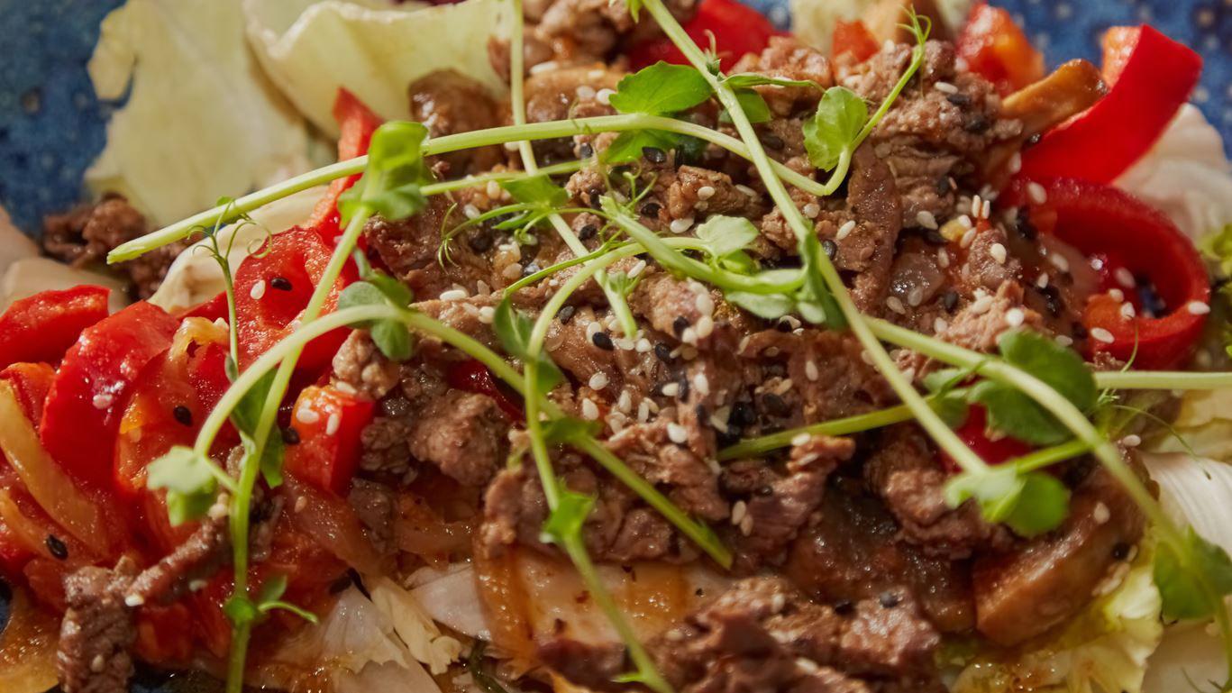 Fried meat with sesame and greens on a blue plate close-up, beshbarmak on a plate with sesame and greens, meat cooked in an oriental style.