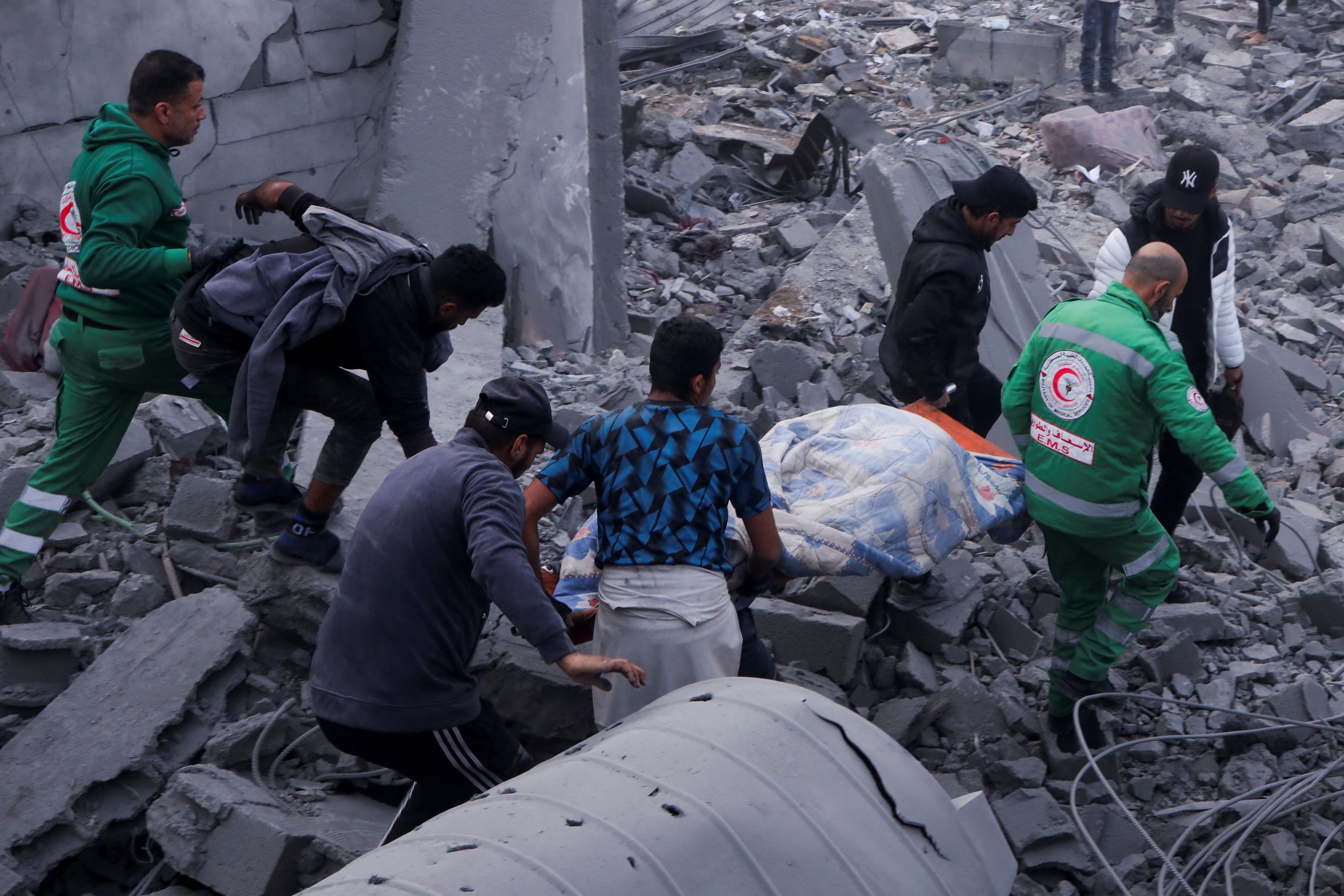 رجال الدفاع المدني ومدنيون يحملون جثمان فلسطيني في موقع غارة إسرائيلية على منازل سكنية، في مدينة غزة، 4 يناير/كانون الثاني 2025