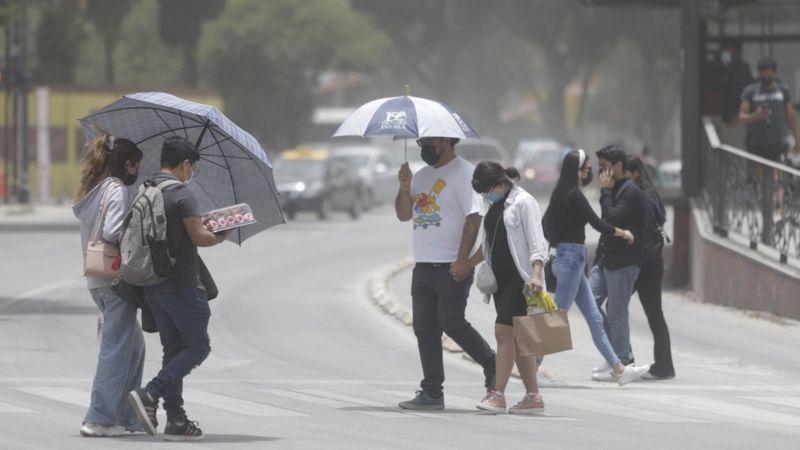 Pessoas de máscara e guarda-chuvas andando pelas ruas de Puebla