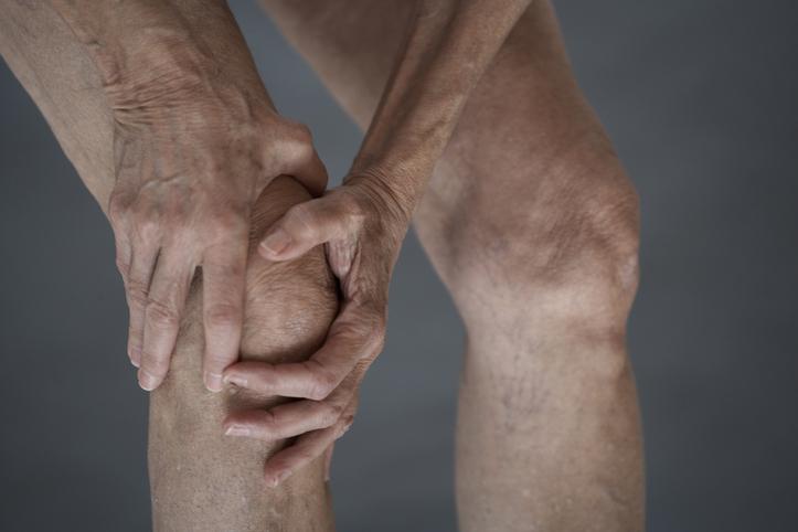 Pessoa com pele envelhecida coloca as mãos no joelho