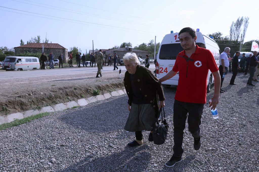 Una señora mayor es acompañada por un voluntario de la Cruz Roja.