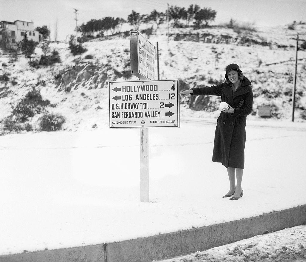 Agnes Strite señalando el cartel de Hollywood 4, LA 12, Hollywood en los años 1930. Vista del lado de las montañas.