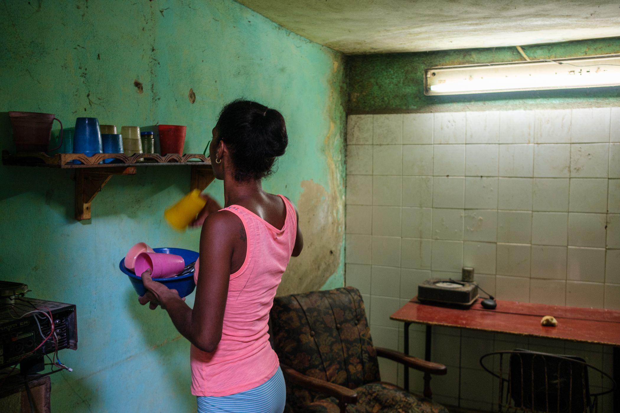 Una madre joven guarda los platos en la cocina de su casa. Vive en un antiguo almacén abandonado, reconvertido en el taller en el que trabaja su marido. Comparten el almacén con otras familias. Este tipo de viviendas suelen ser pequeñas, sobrepobladas y con un deterioro que refleja años de dificultades económicas.