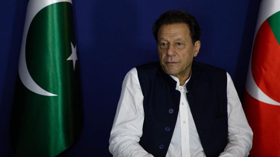 Imran Khan sitting next to a Pakistan flag