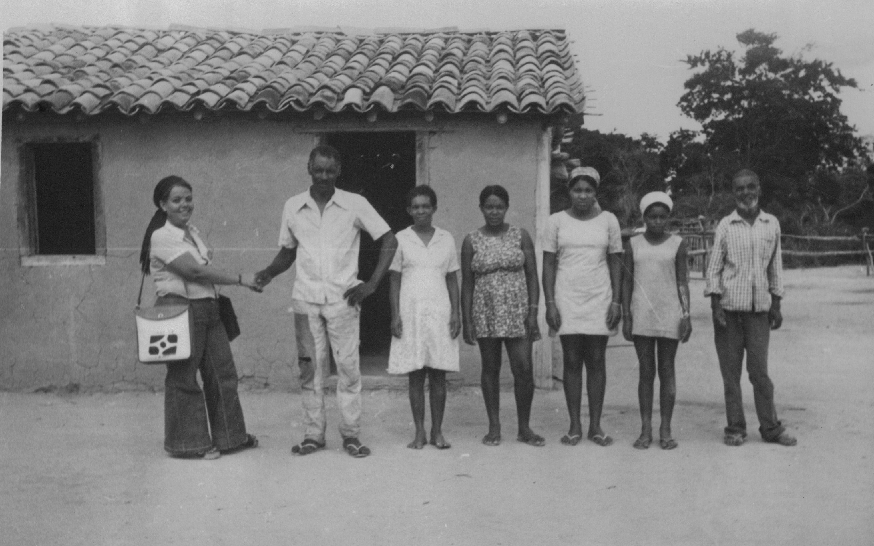 Pesquisadora do IBGE posa com família pesquisada em frenta a sua residência