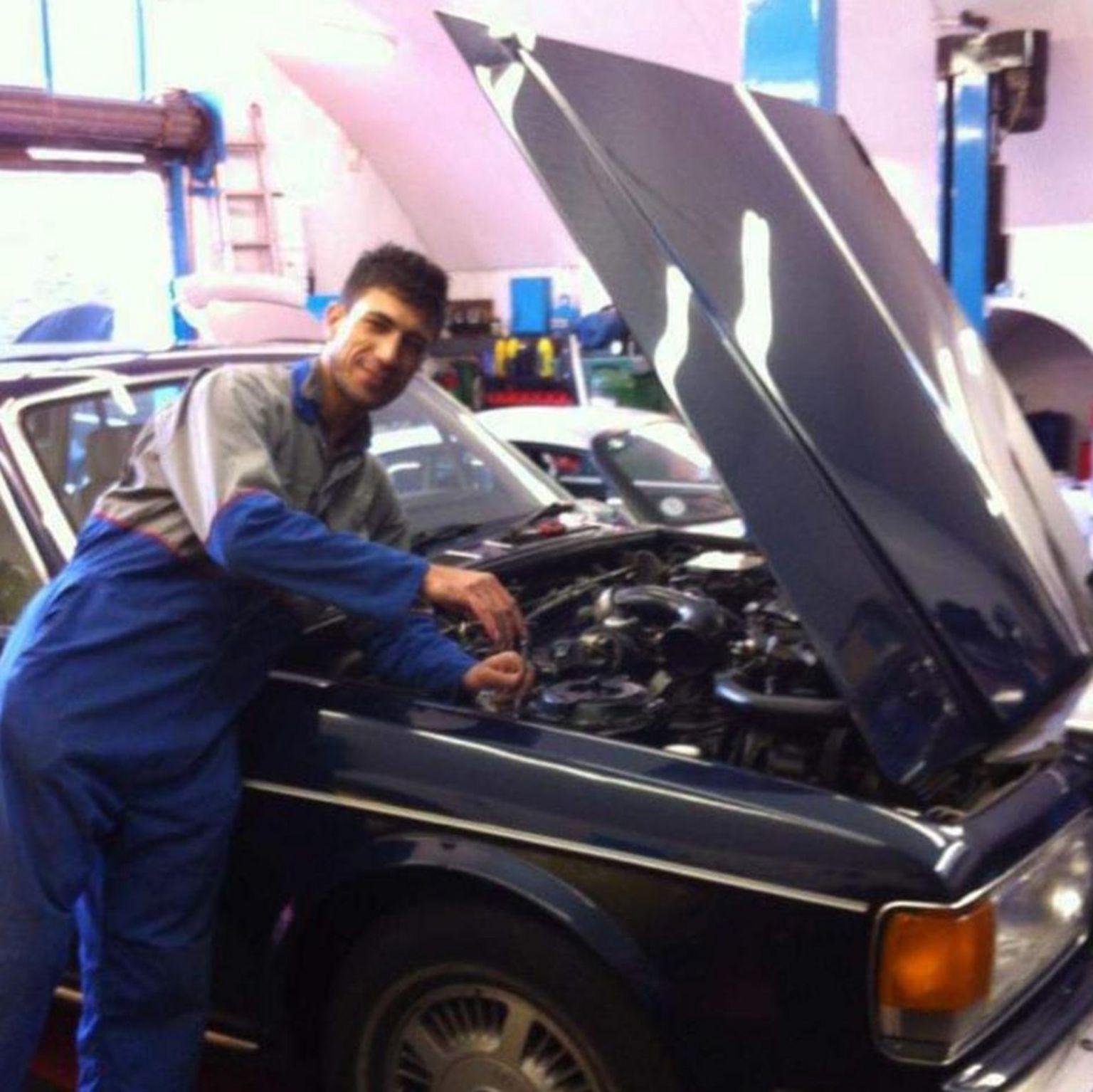 Majeed com roupa de mecânico, perto de capô de carro 