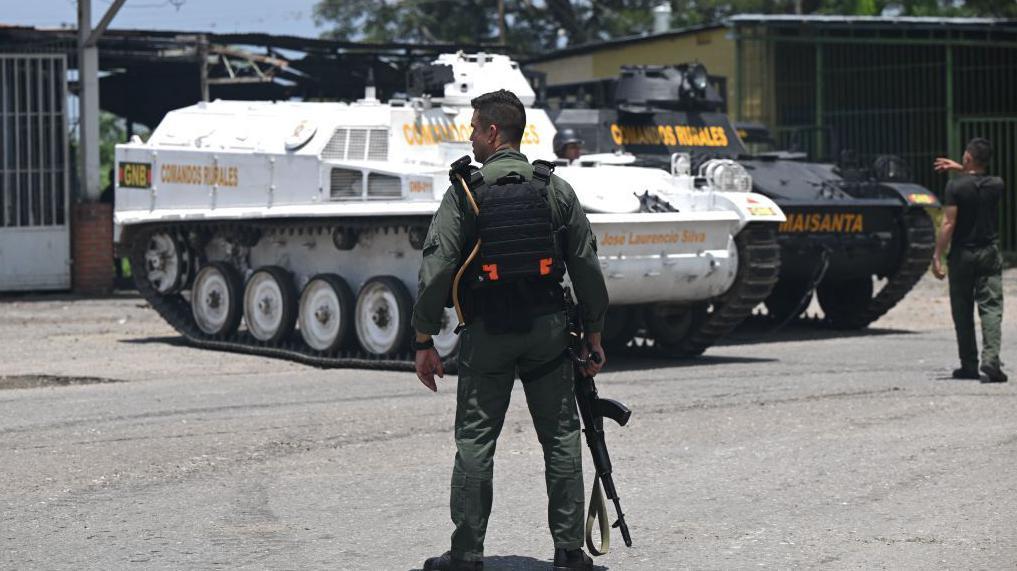 Un miembro de la Guardia Nacional Bolivariana de Venezuela parado frente a dos vehículos blindados durante el operativo para ingresar en cárcel de Tocorón